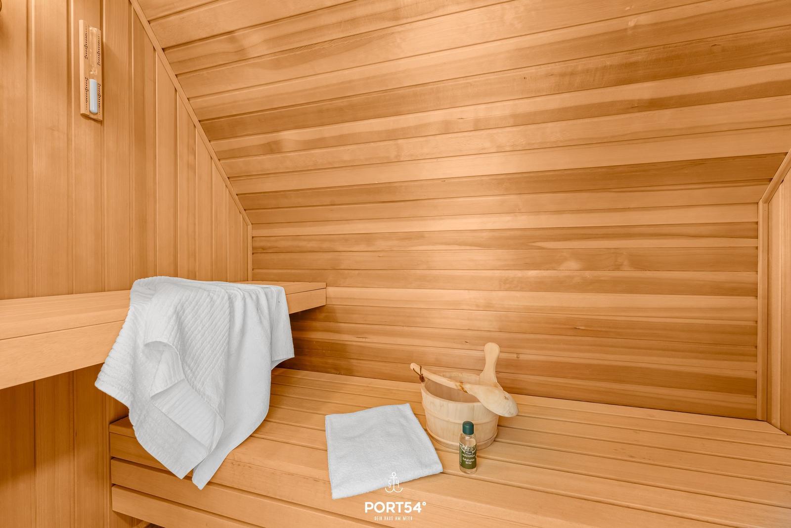 Sauna mit Holzbank, Handtuch und Eimer mit Löffel.