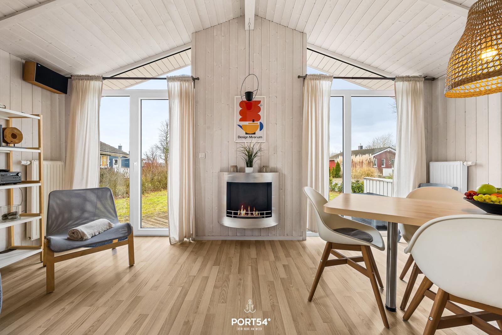Wohn- und Essbereich mit Kamin, Tisch, Stühlen und Blick auf Garten.