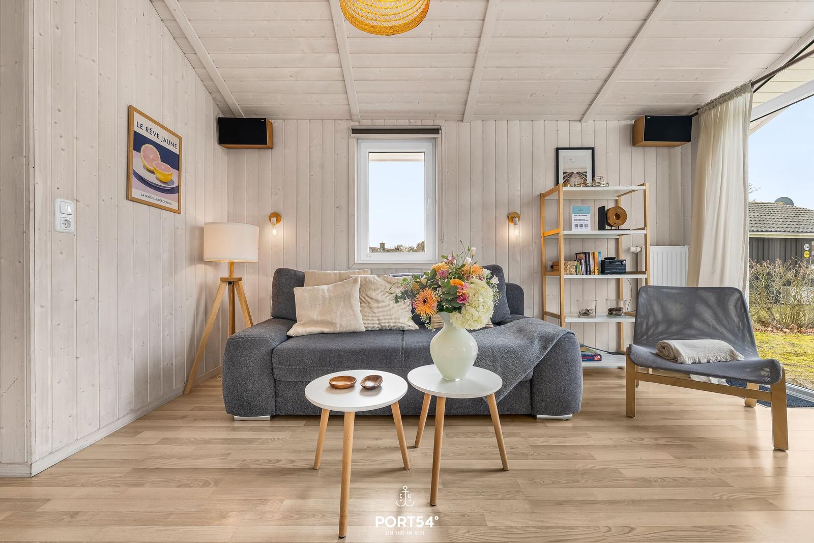 Wohnzimmer mit grauem Sofa, Holzboden und Fenster zur Aussicht.