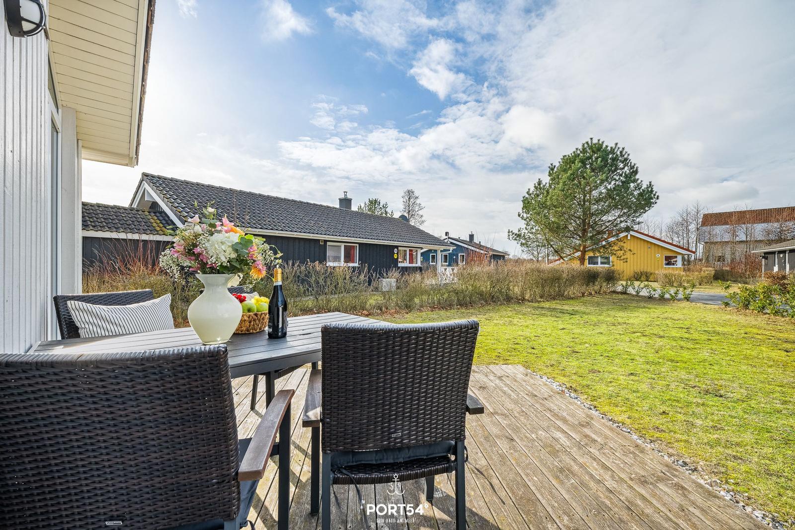 Terrasse mit Tisch, Stühlen und Blumen. Blick auf grünen Rasen und Nachbarhäuser.