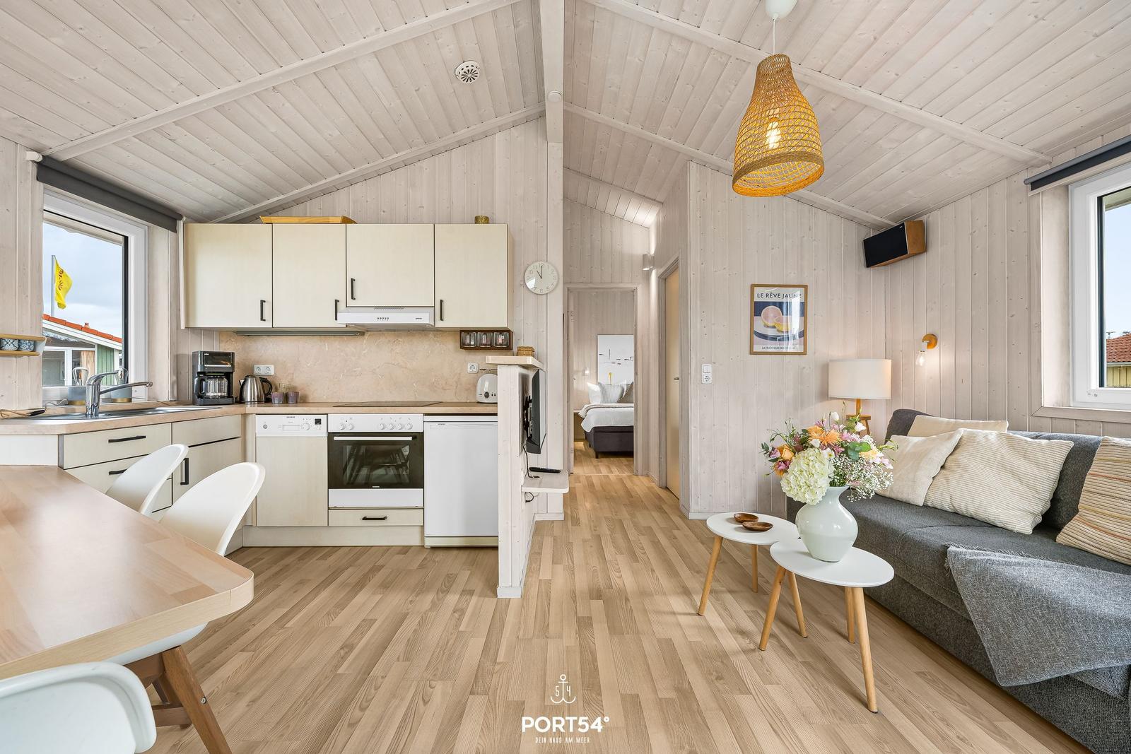 Wohnküche mit Sofa, Tisch und Küchenschränken. Holzdecke und -boden.