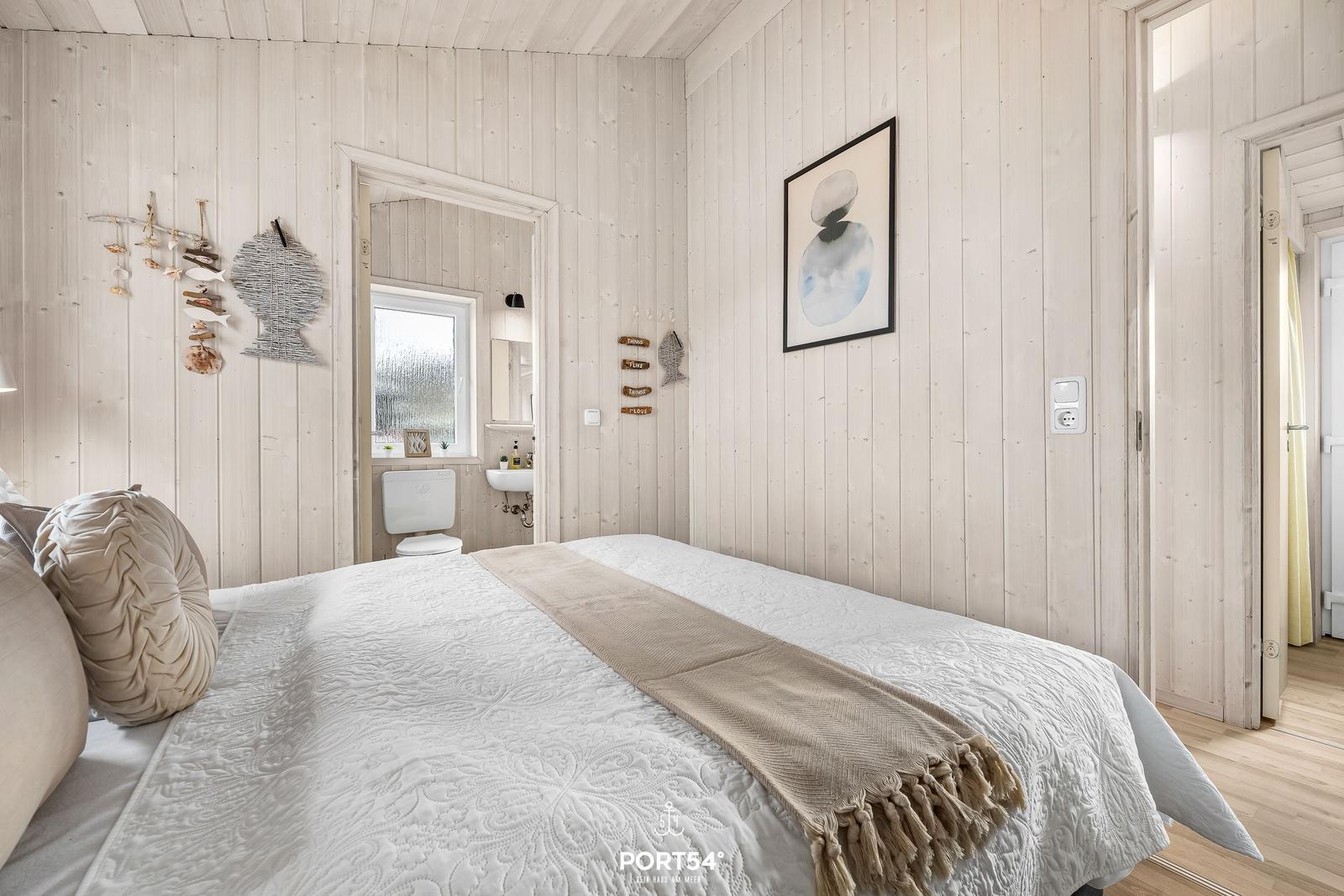 Schlafzimmer mit Bett, Holzwand und Blick in Badezimmer.