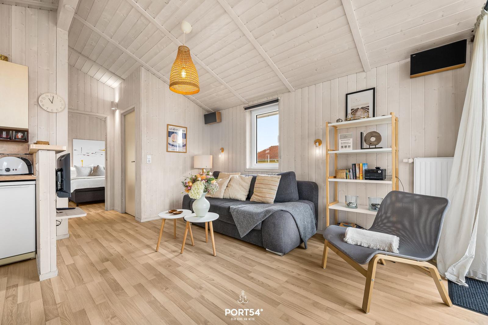 Wohnbereich mit Sofa, Sessel und Küchenzeile in einem Holzhaus.
