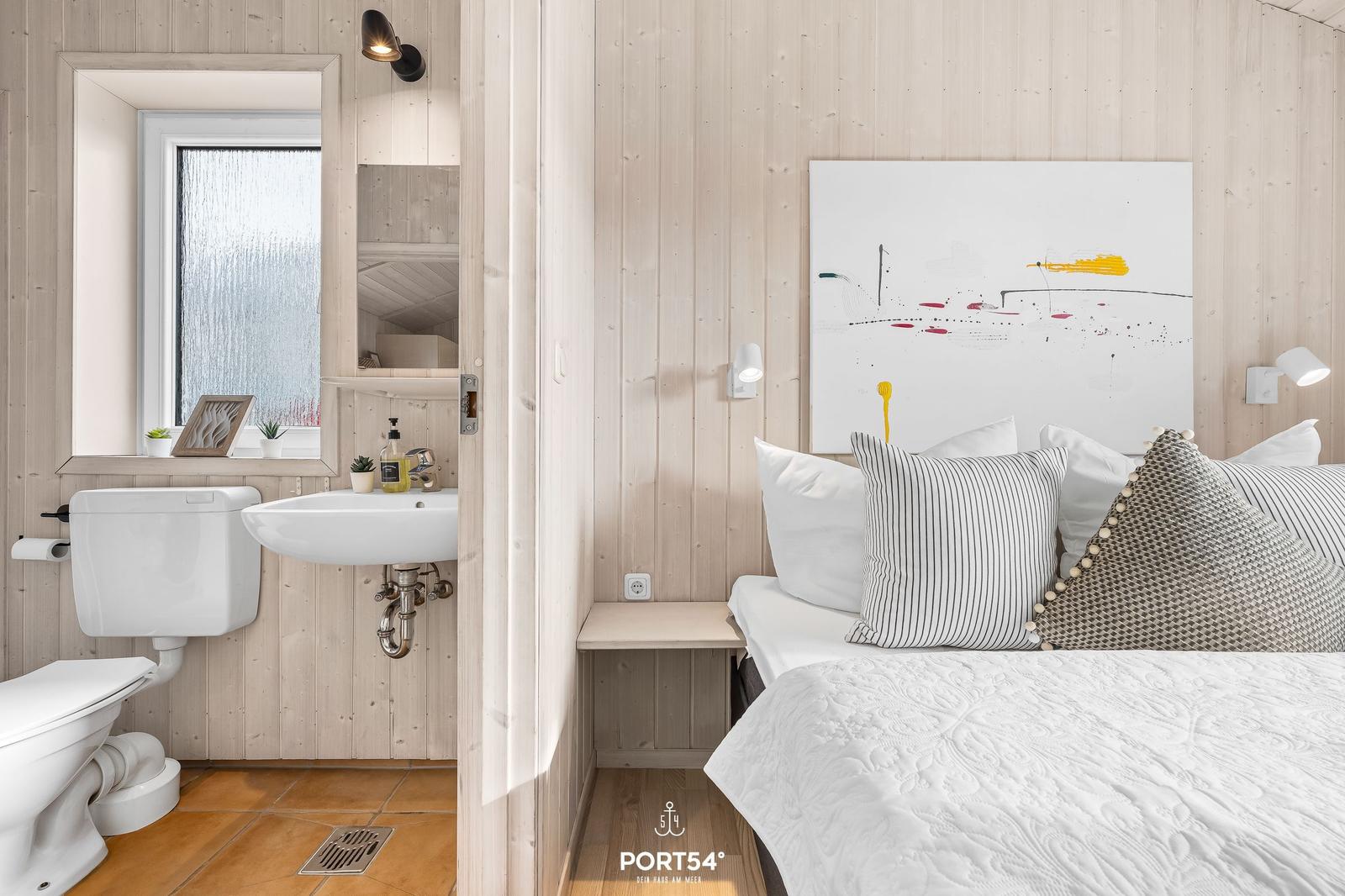 Schlafzimmer mit Bett und Wandbild. Nebenraum mit Toilette und Waschbecken.
