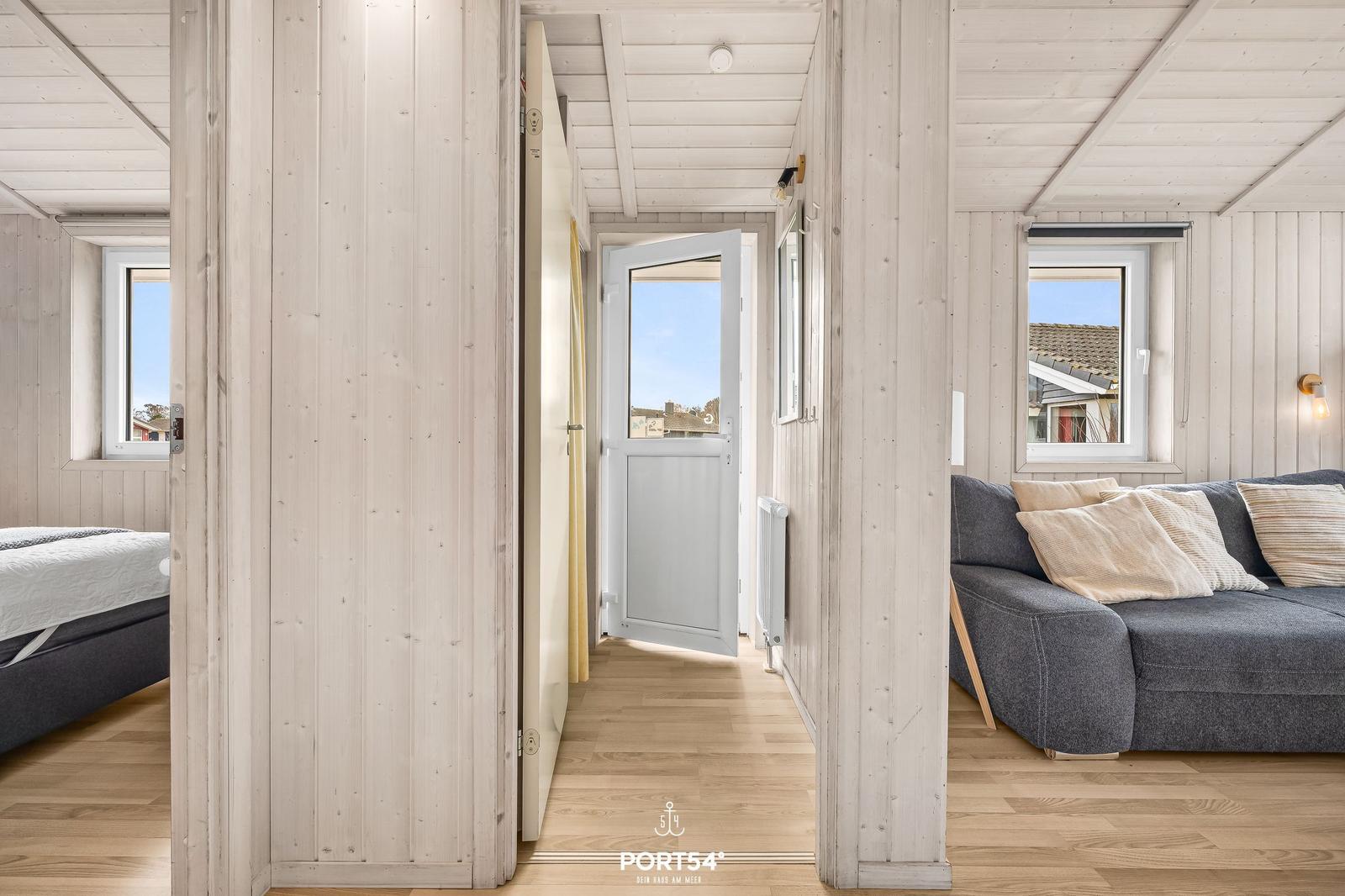 Flur mit Schlafzimmer und Wohnzimmer, Holzwände, offene Tür, Sofa mit Kissen.
