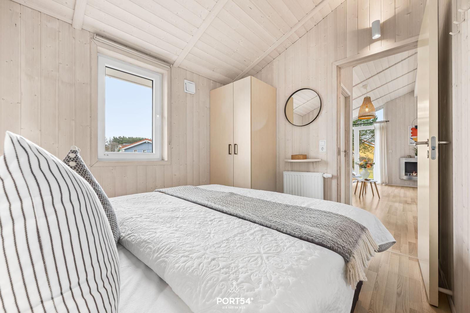 Schlafzimmer mit Bett, Kleiderschrank und Fenster. Durchgang zur Wohnfläche mit Kamin.