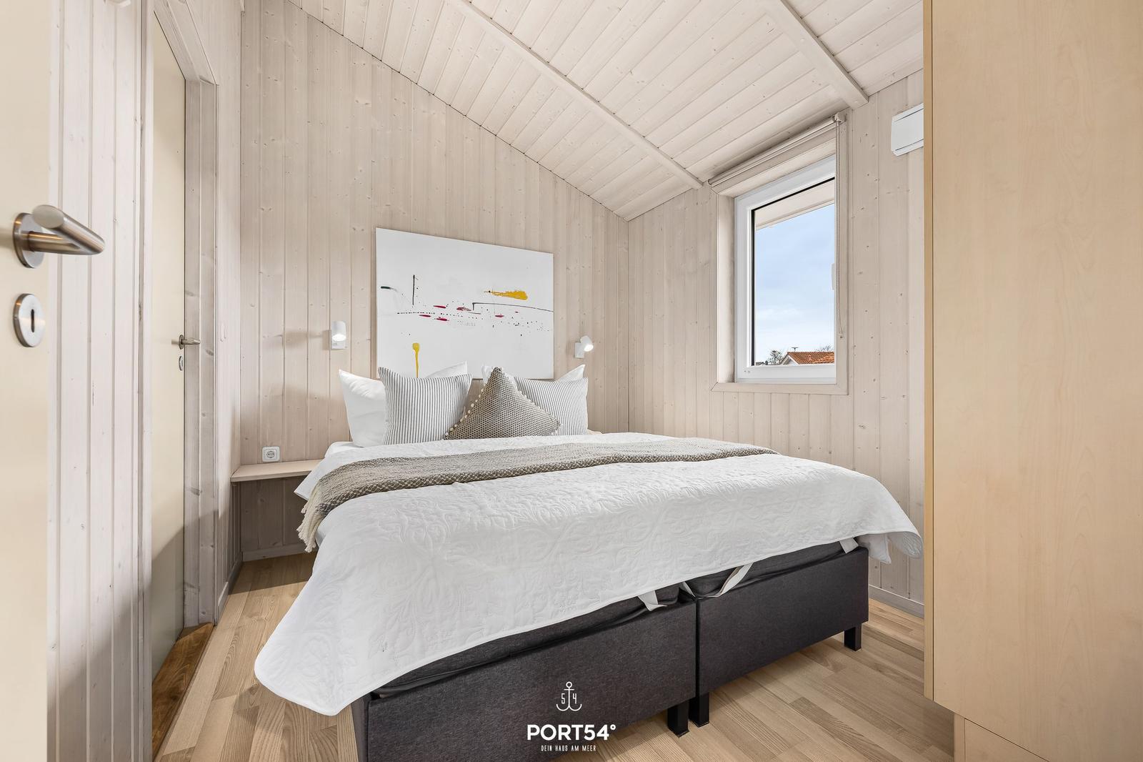 Schlafzimmer mit Bett, Wandbild und Fenster. Holzwände und Boden.