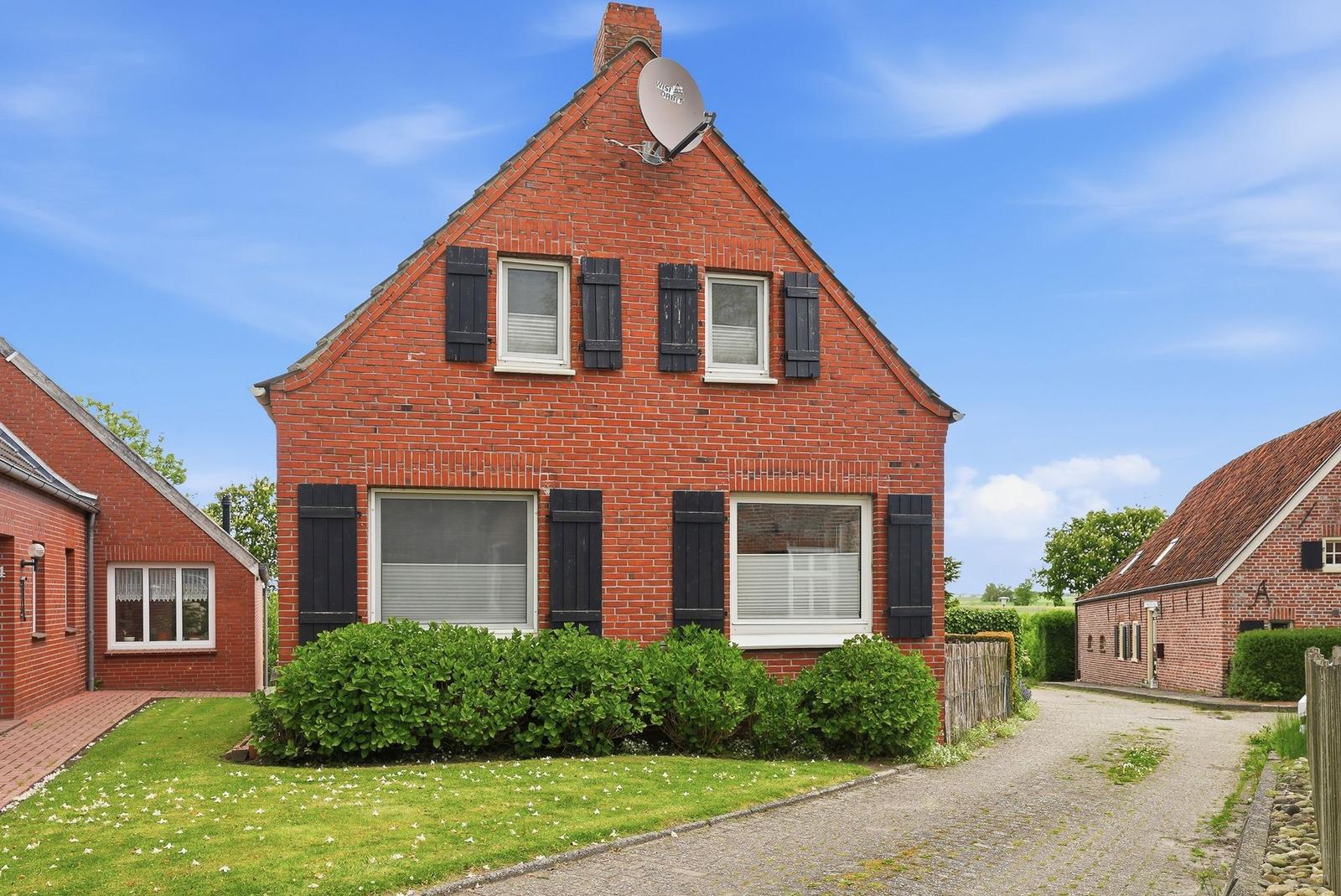 Red brick house with black shutters and satellite dish under blue sky.