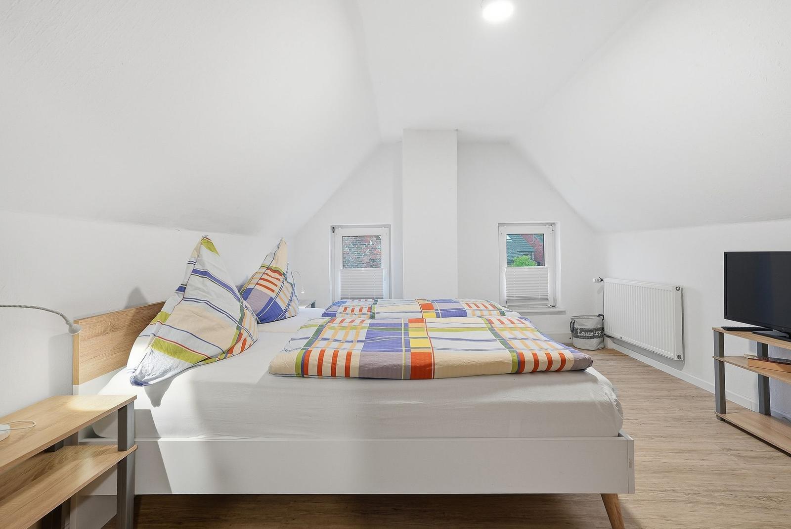 Bedroom with double bed, two windows, and TV.