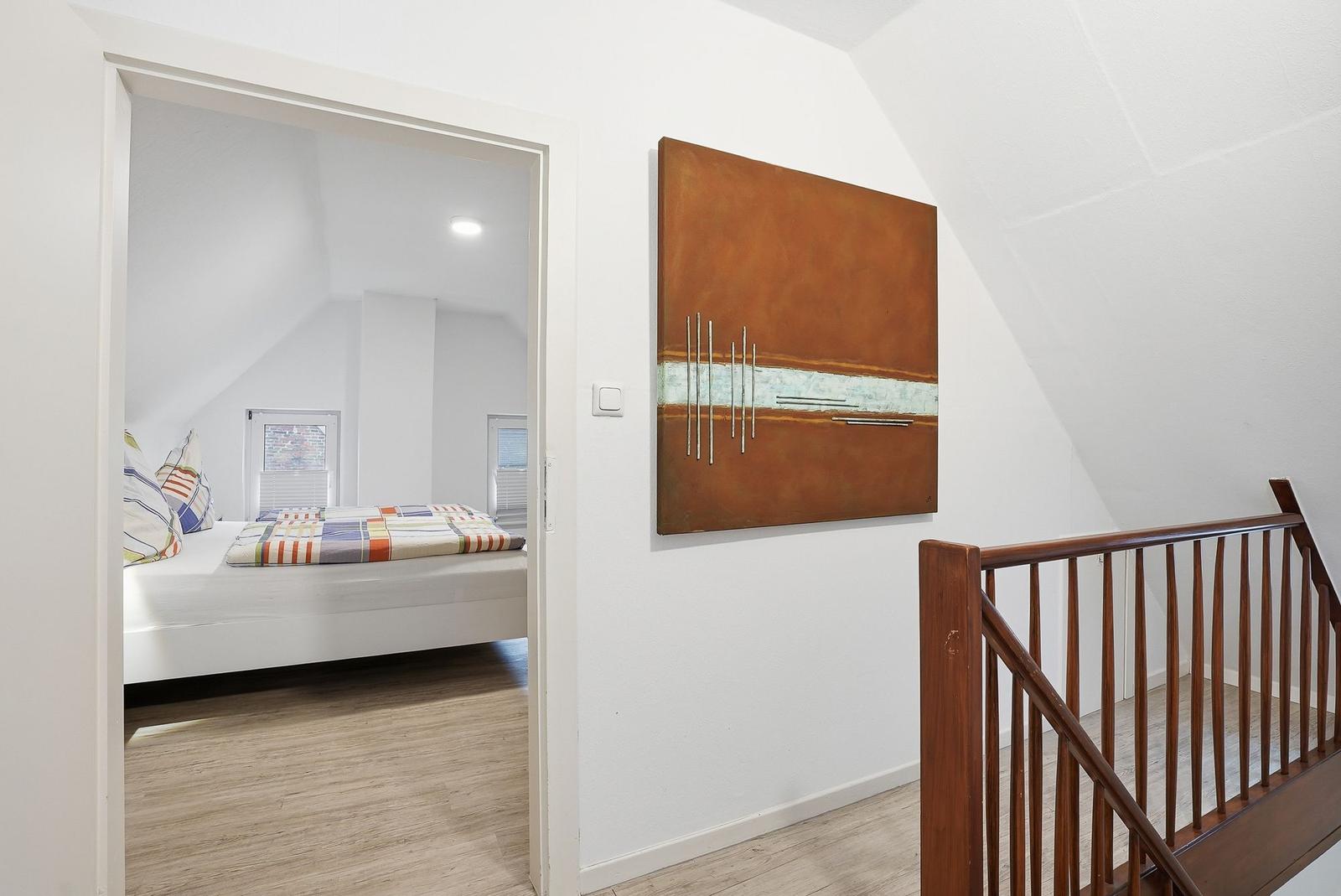 Bedroom with bed and windows, wall art and wooden railing visible.