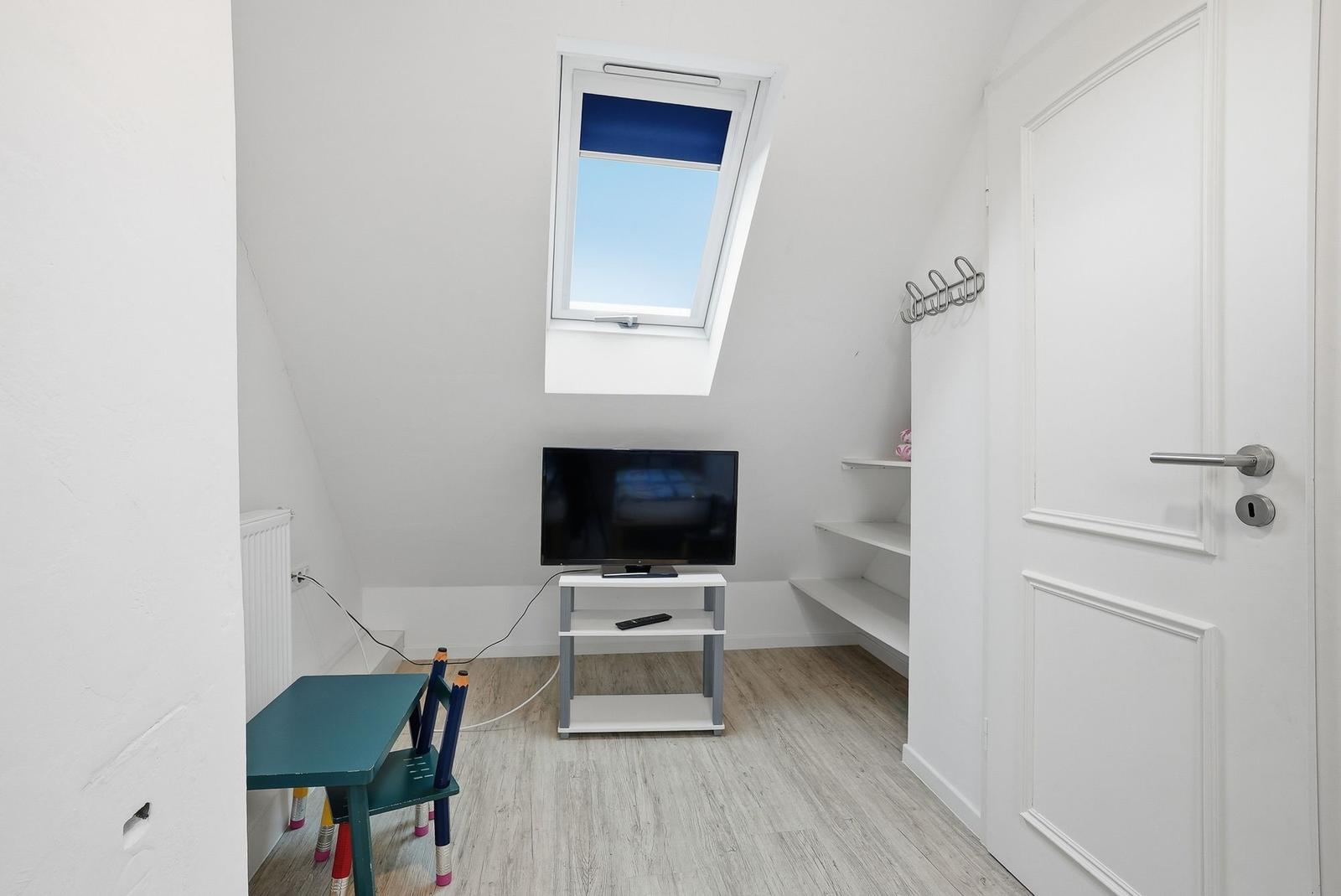Bedroom with skylight, TV, and childrens table. White walls and wooden floor.
