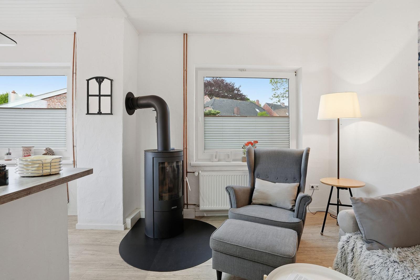 A living room with a gray armchair, wooden floor, and a black wood stove.