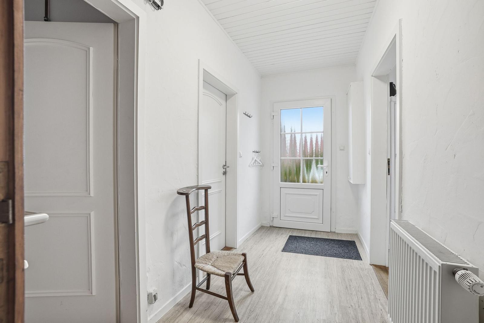 Hallway with white walls, wooden floor, and door to outside area.