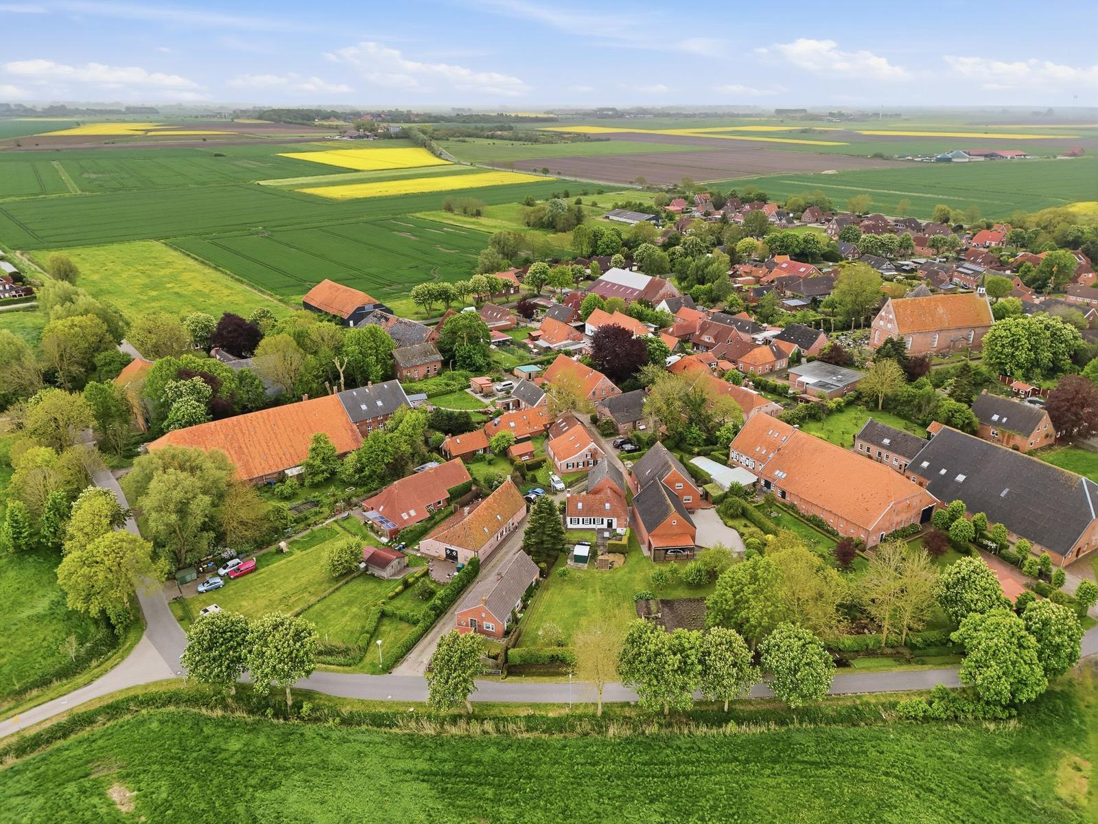 Aerial view of a village with red-tiled roofs, surrounded by green fields and yellow rapeseed.