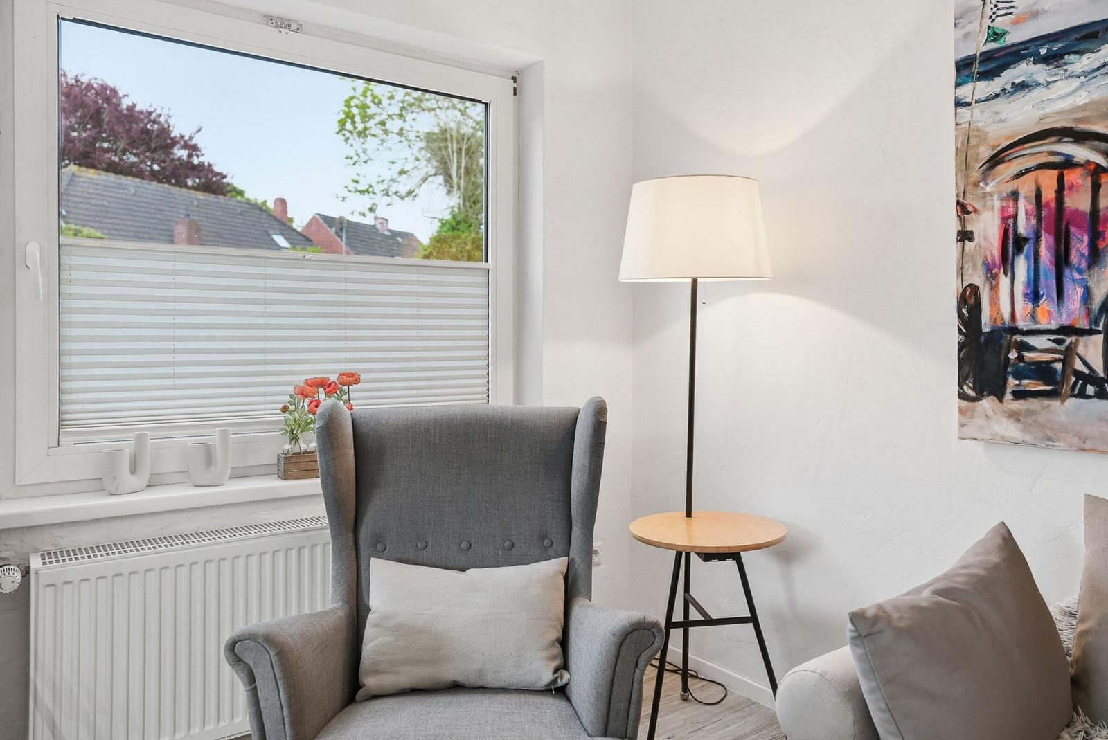 A gray armchair with a cushion is near a window with blinds. A floor lamp stands beside it.