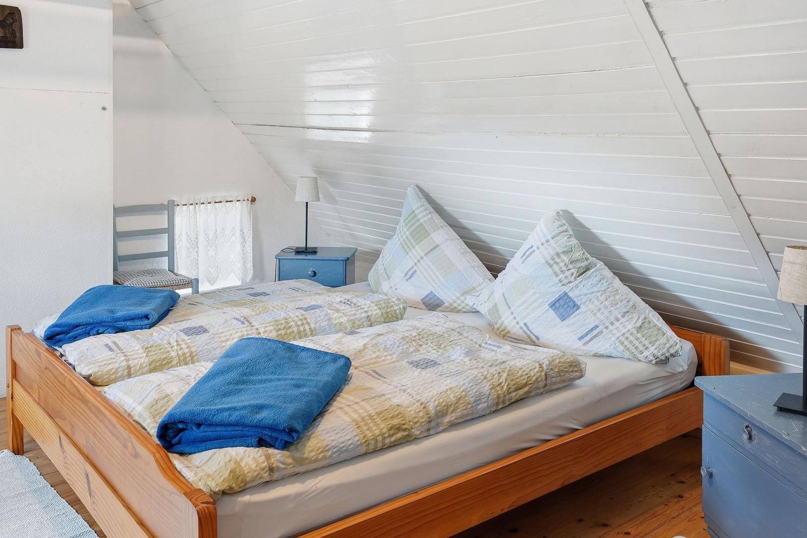 Schlafzimmer mit Doppelbett, blauen Nachttischen und schrägem Dach