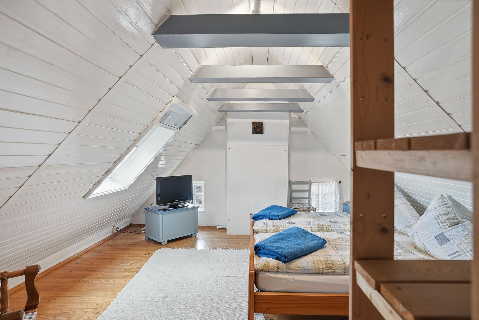 Schlafzimmer mit Dachschrägen, Bett, Fernseher und Fenster