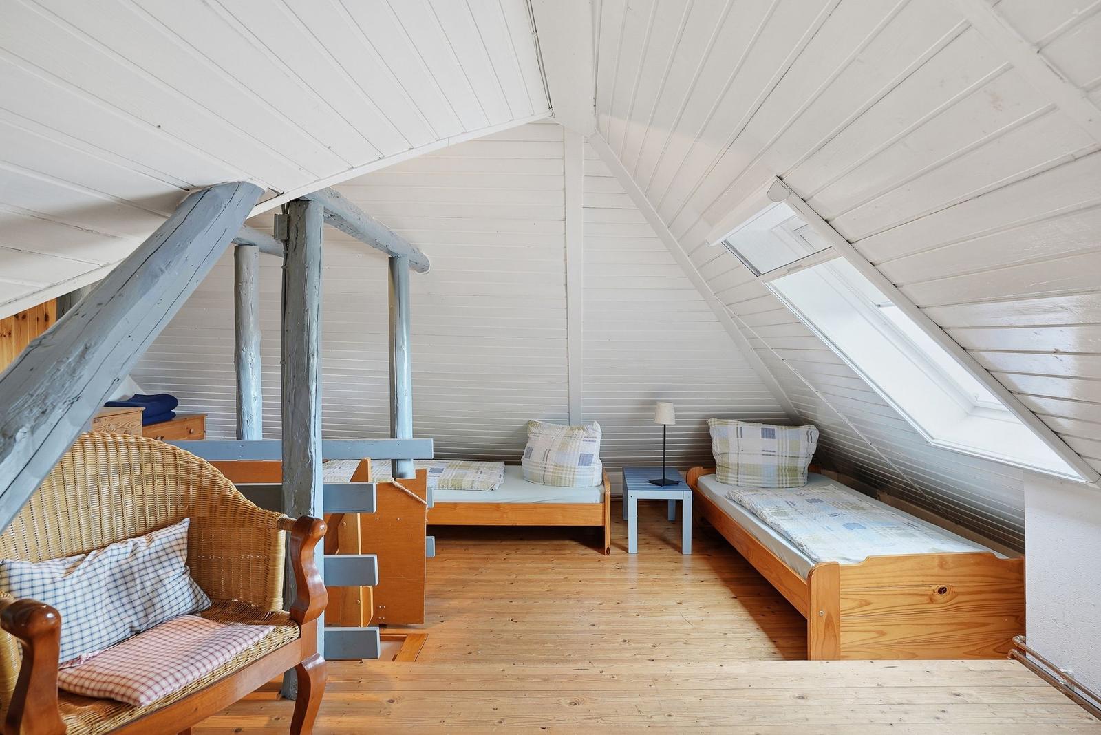 Zimmer mit zwei Betten, Sitzgelegenheit und Dachfenster. Holzdecke und -boden.