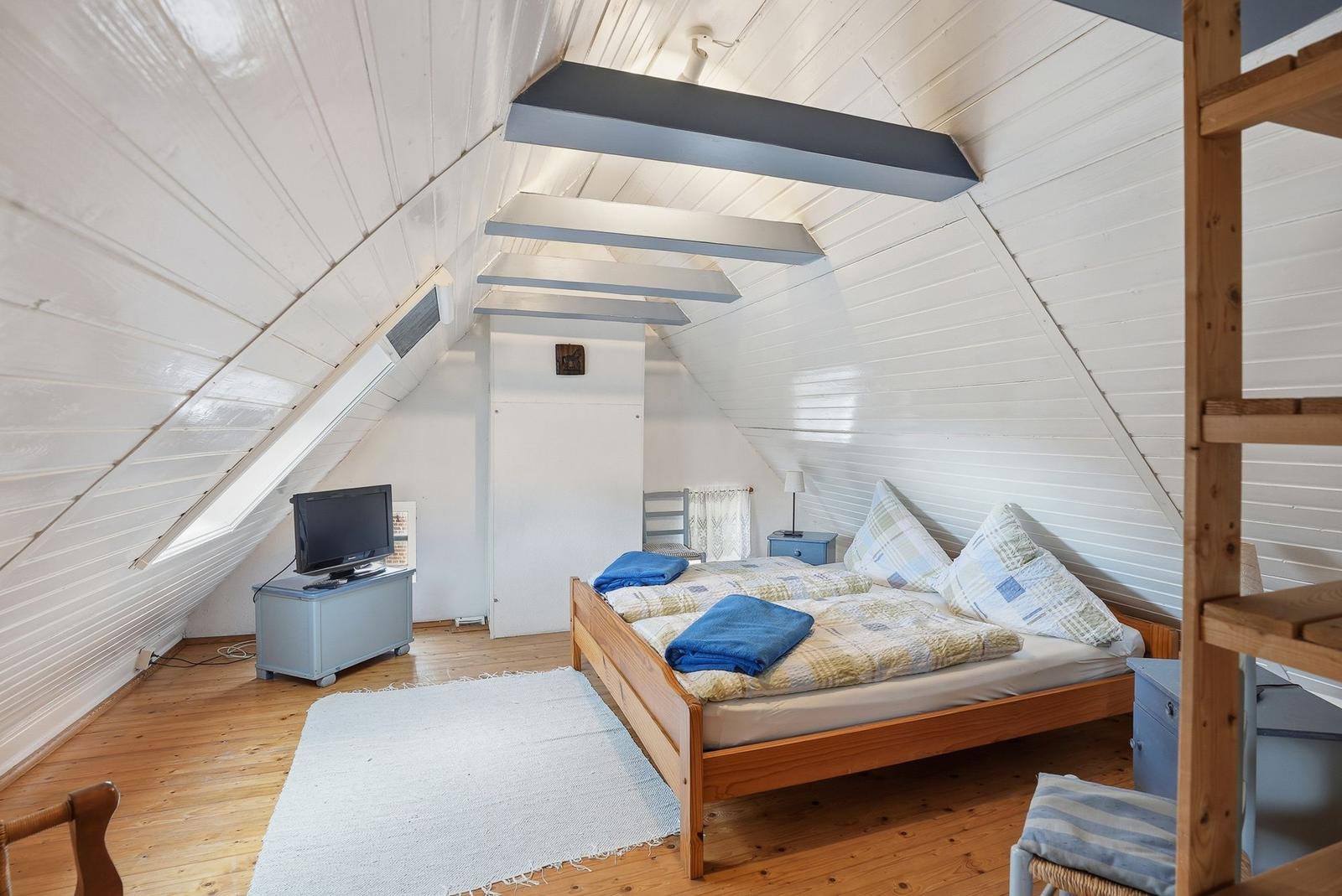 Schlafzimmer mit Holzboden, Bett, Fernseher und Dachschrägen.