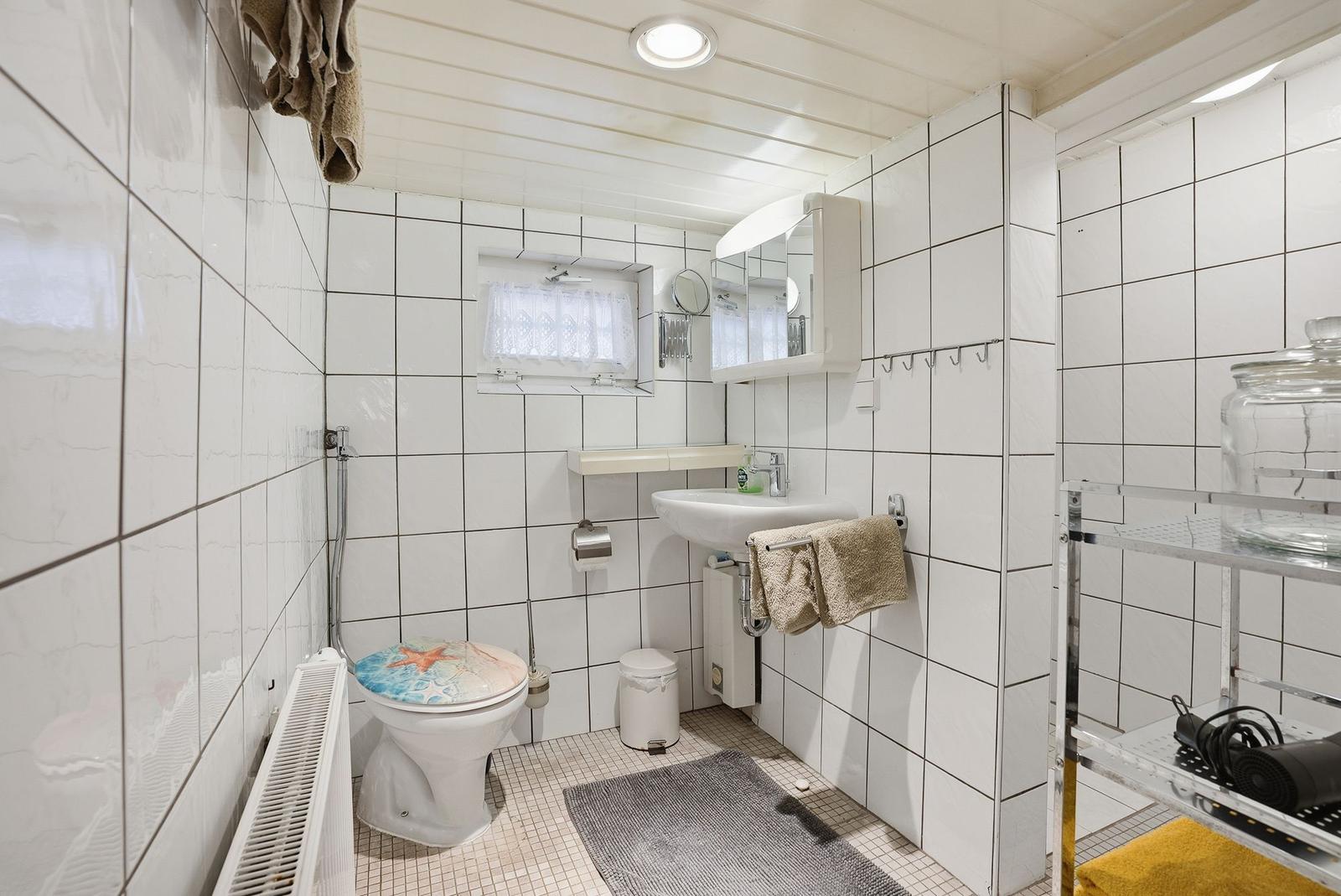 Badezimmer mit Toilette, Waschbecken und Dusche. Weiße Fliesen und Handtuchhalter sichtbar.