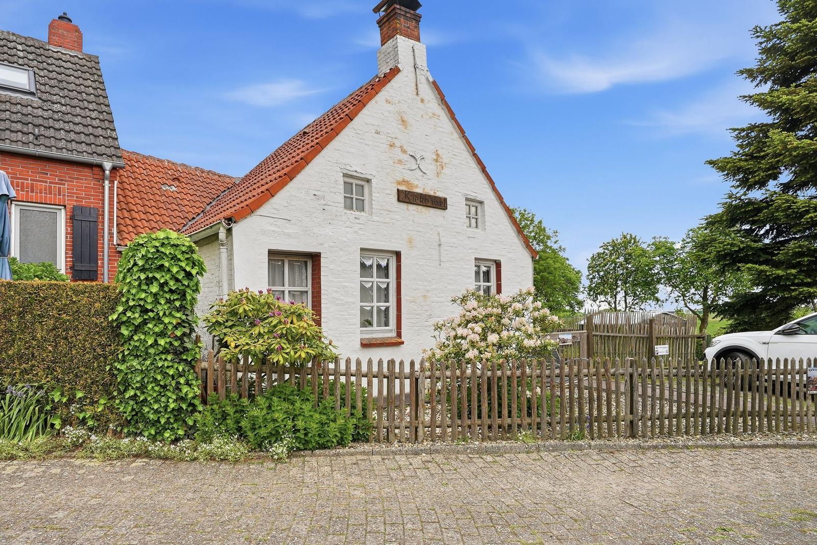 Weiße Fachwerkhäuser mit rotem Dach und Holzzaun. Garten mit Blumen und Bäumen.