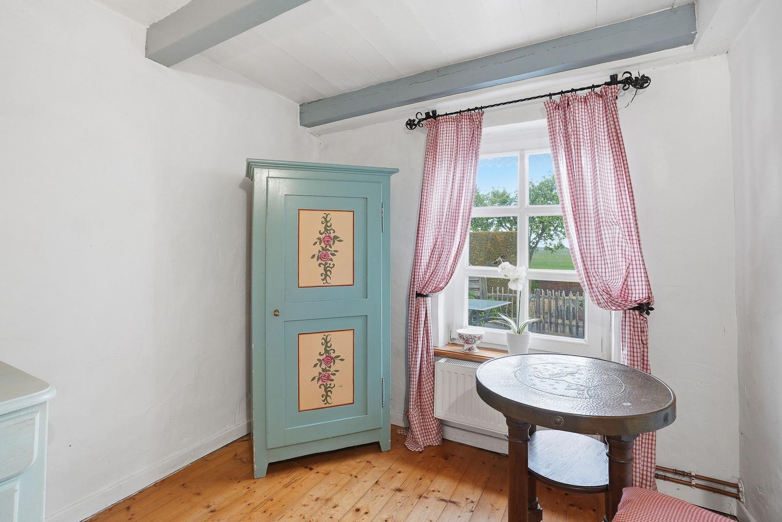 Ein Raum mit Holzboden, blauem Schrank und roten Gardinen vor dem Fenster.