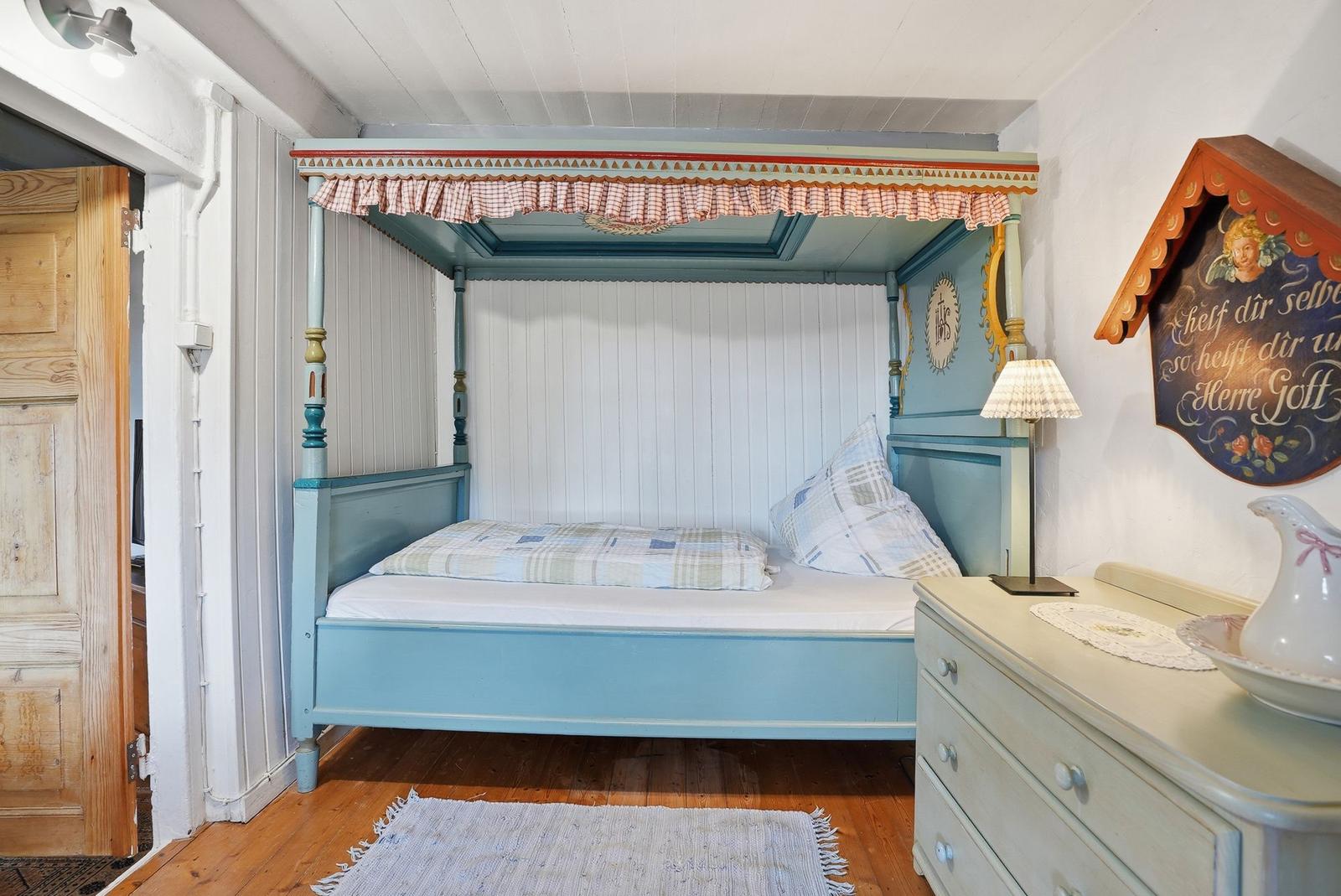 Ein Schlafzimmer mit einem blauen Himmelbett, einem Schrank und einer Holztür.