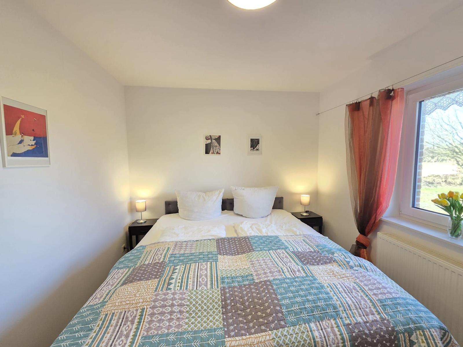 Schlafzimmer mit Doppelbett, zwei Nachttischen und Fenster mit Blumen.