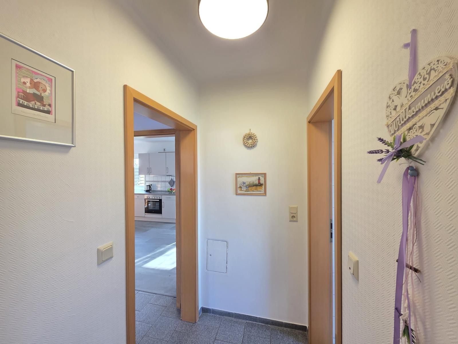 Flur mit Küchen- und Türöffnung, Wandbild und Herzdekoration mit Willkommen.