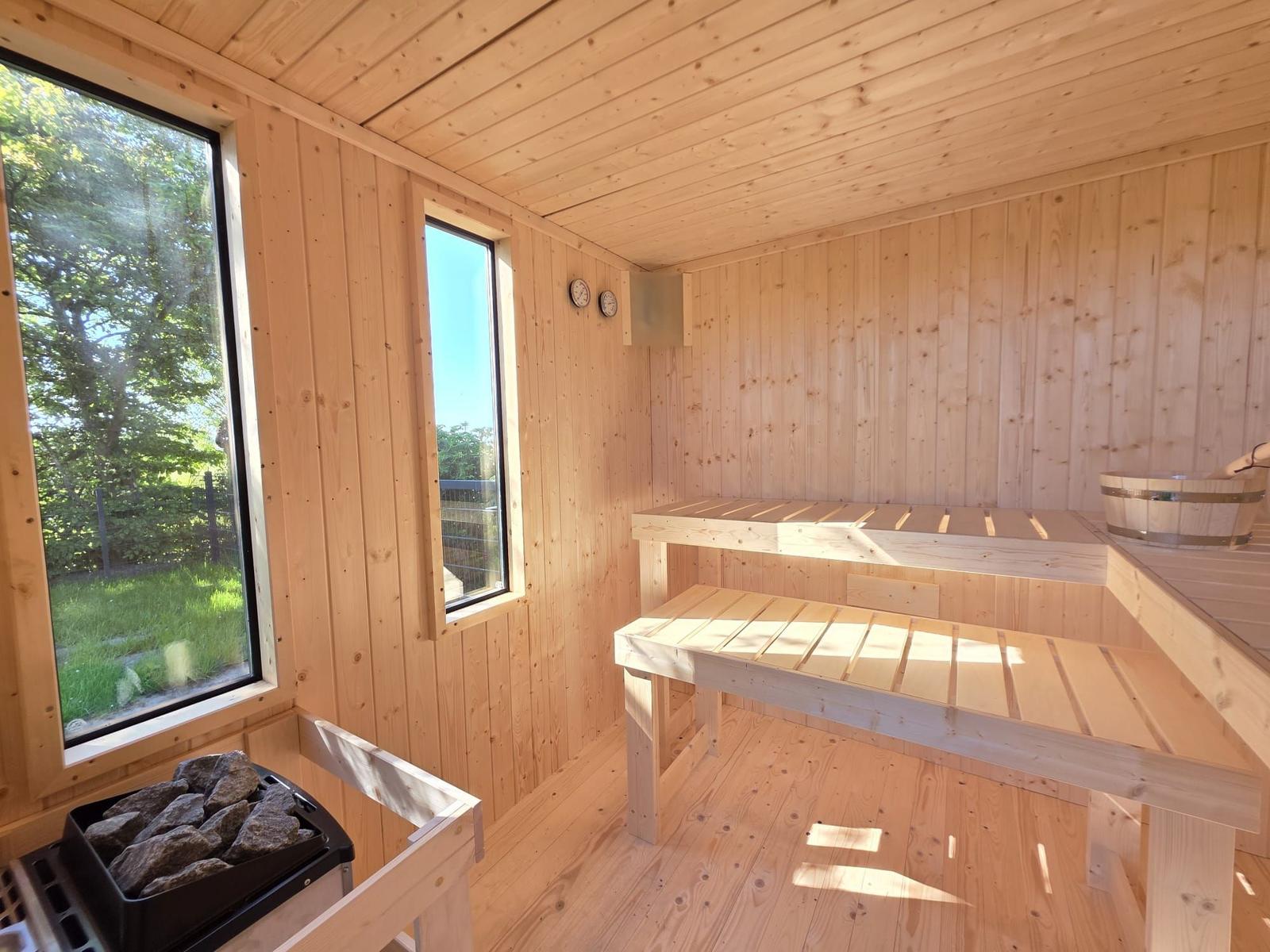 Holzsauna mit Sitzbänken, Fenstern und Steinheizung.