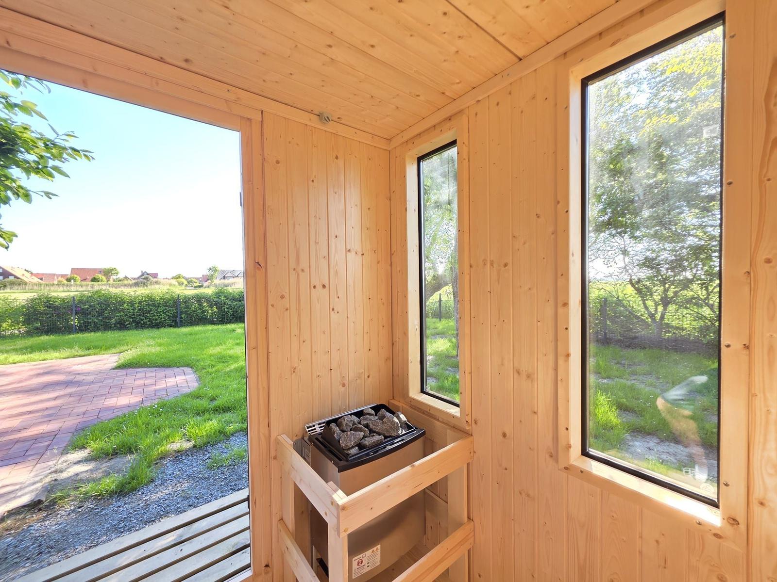 Holzsauna mit Steinheizung und Blick auf Garten.