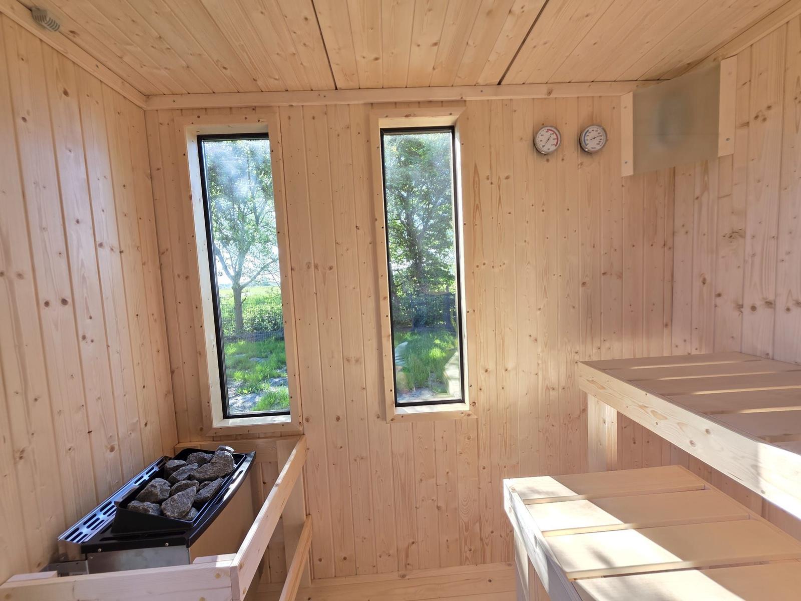 Sauna mit Holzwand, zwei Fenstern und Steinbodenheizung.