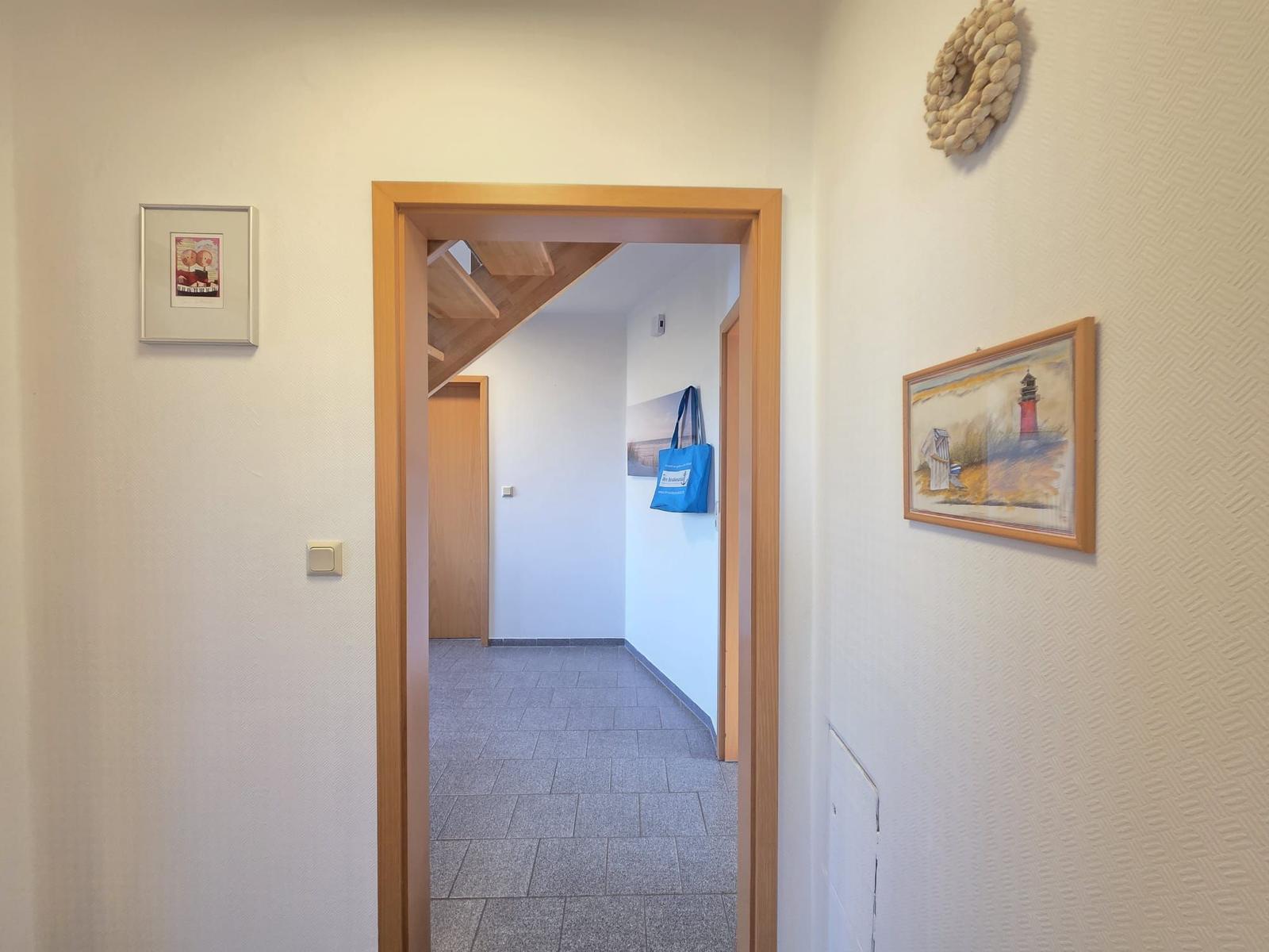 Hausflur mit Holztür, Wandbildern und Blick in den Flur mit Treppe.
