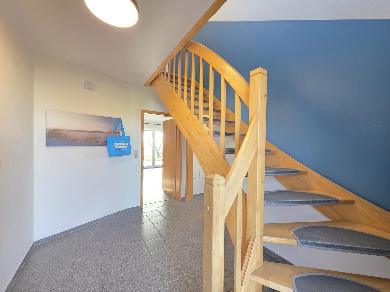 Holz-Treppe mit blauer Wand und Wandbild. Bodenfliesen und Tür im Hintergrund.