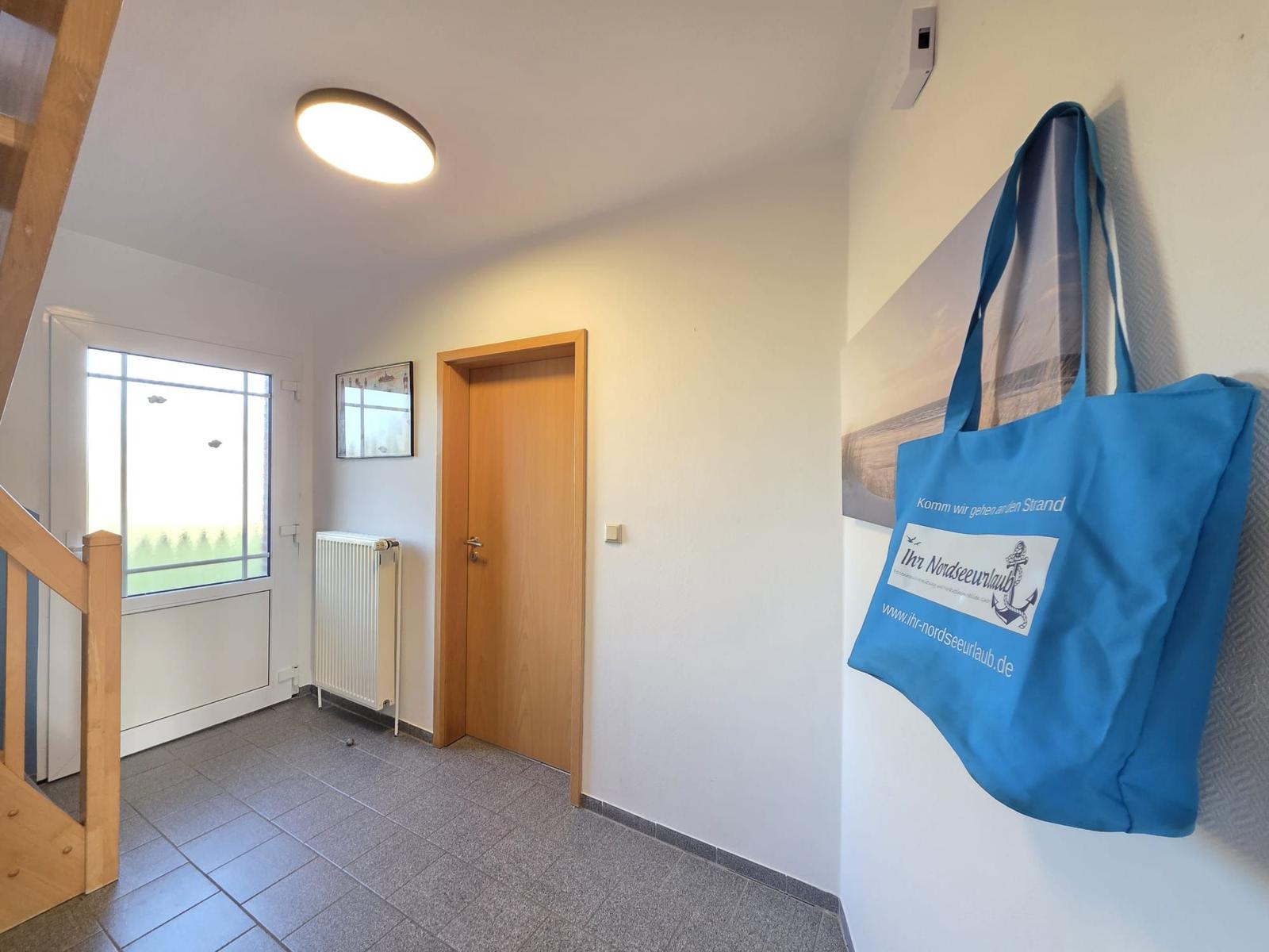 Eingangsbereich mit Tür, Fenster und blauer Strandtasche an der Wand.