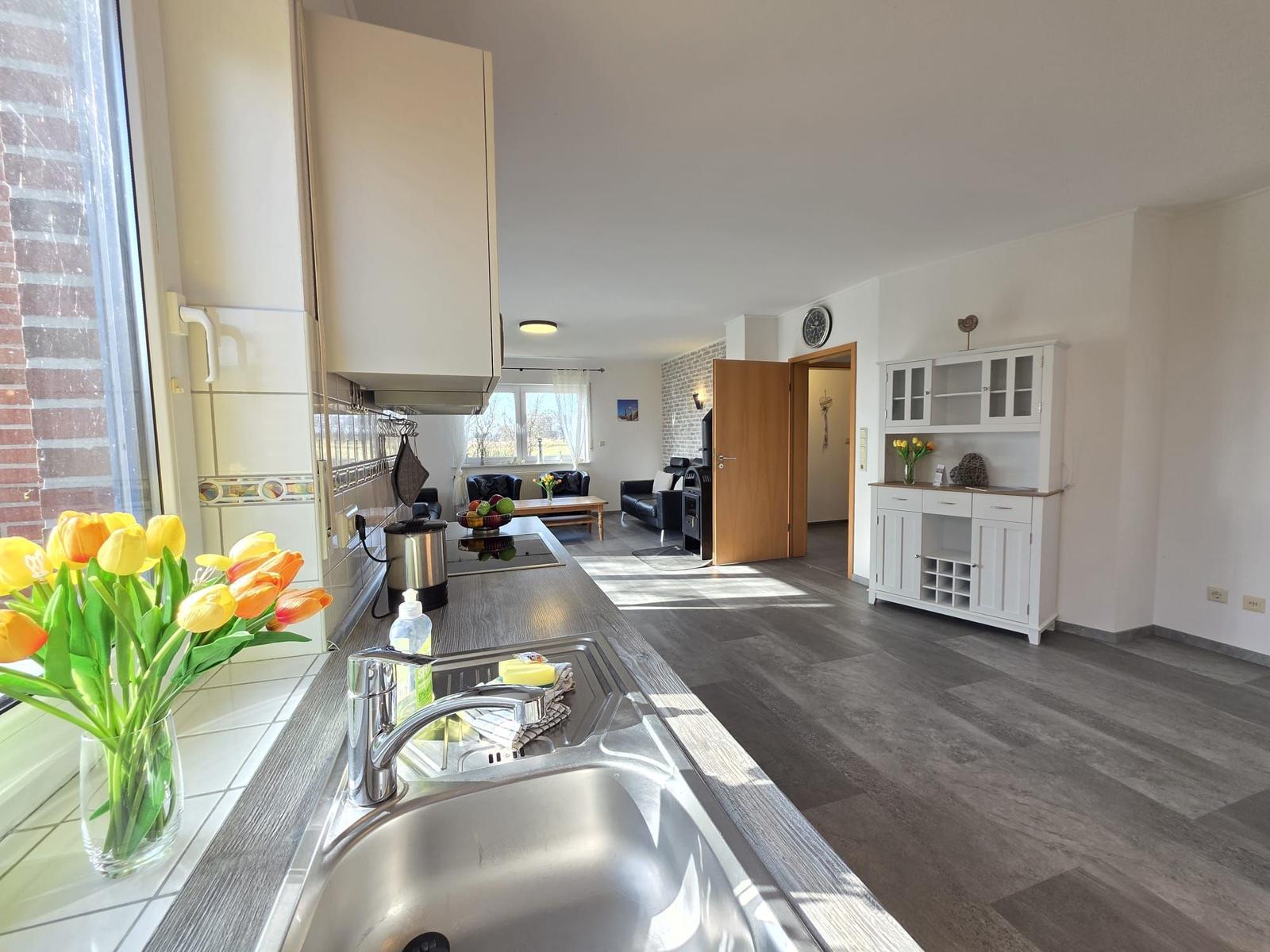 Küche mit Arbeitsplatte, Spüle und Fenster. Blick in Wohnzimmer mit Sofa und Kamin.