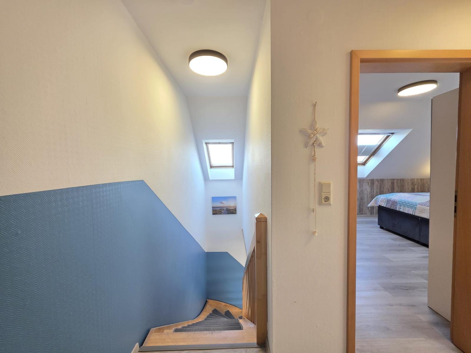 Treppenhaus mit blauer Wand und Blick in Schlafzimmer mit Dachfenster.