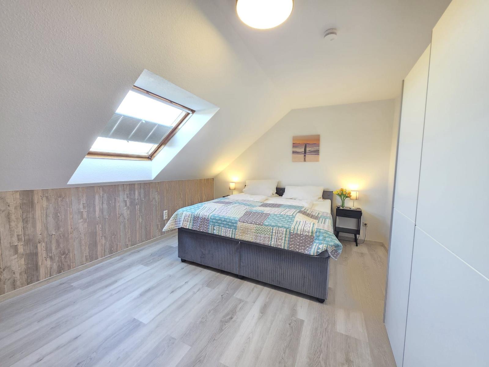 Schlafzimmer mit Dachschrägen, Dachfenster, Bett und Nachttisch.