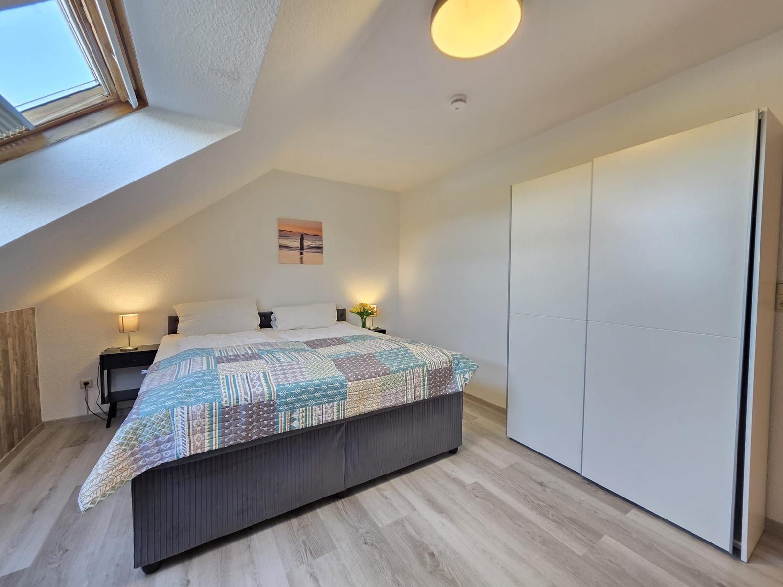 Schlafzimmer mit Dachschrägen, Doppelbett, Kleiderschrank und Dachfenster.