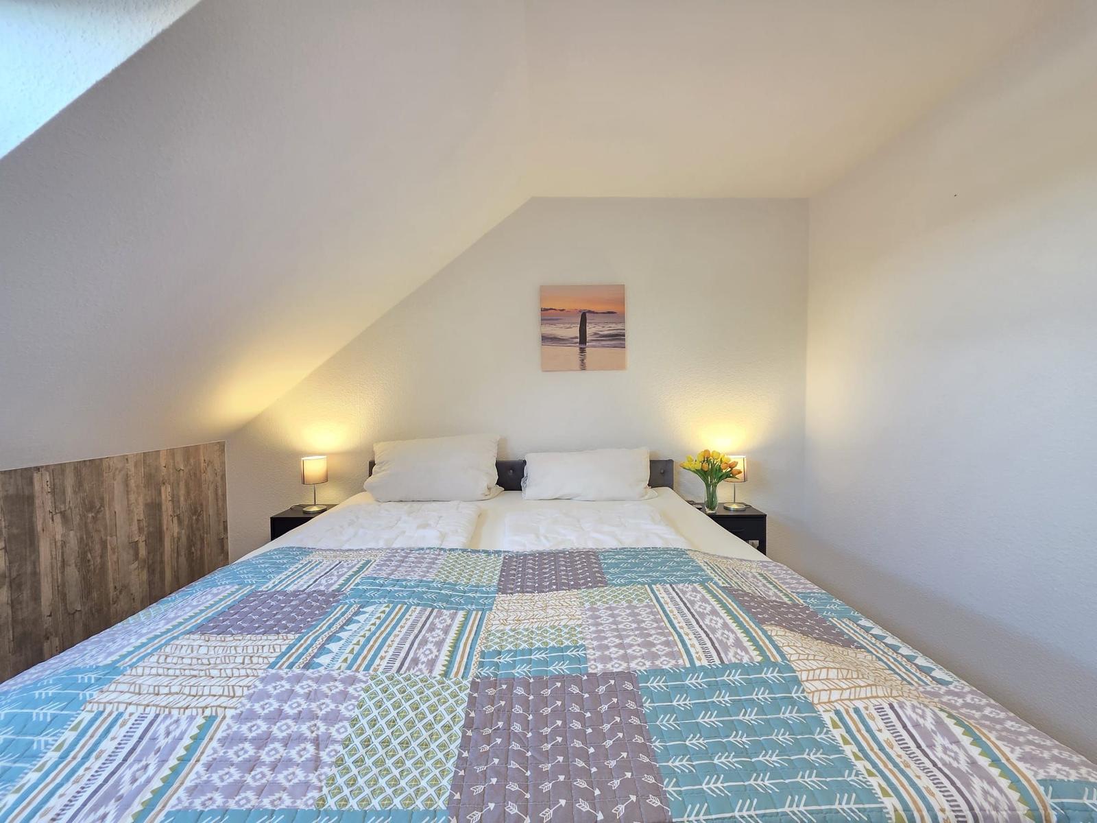 Schlafzimmer mit Doppelbett, zwei Nachttischen und Wandbild.