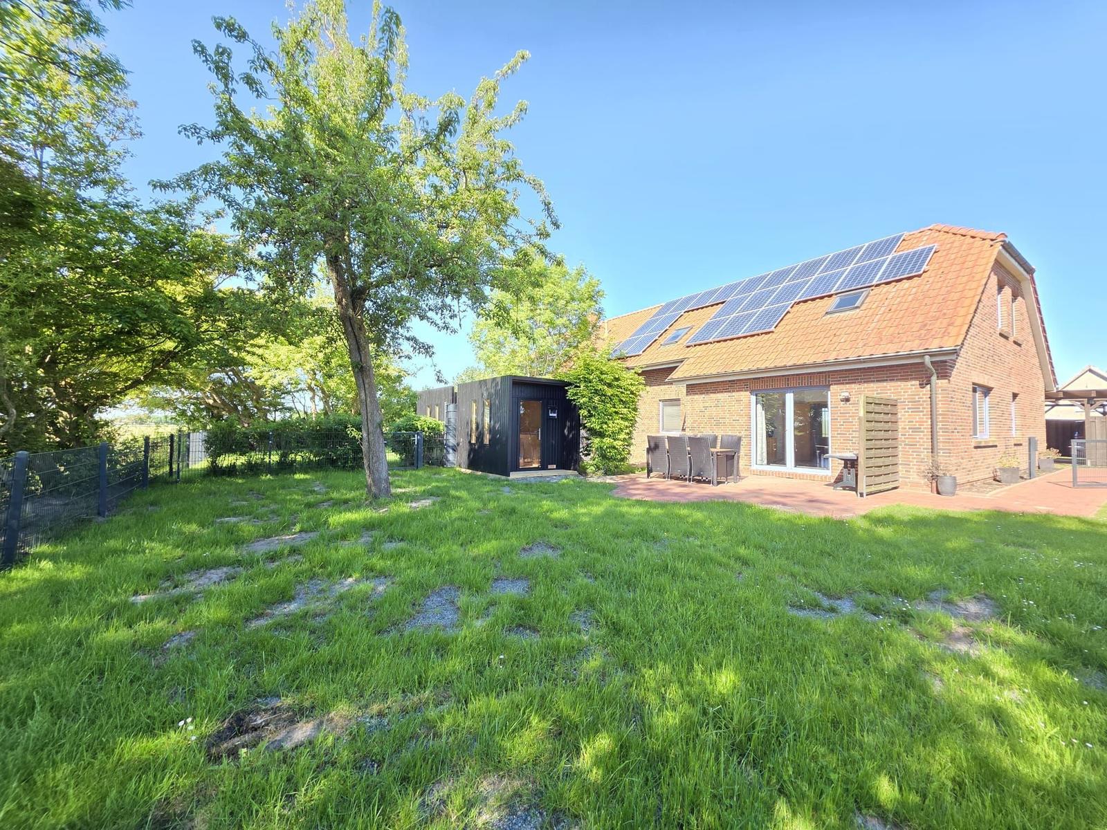 Haus mit Solaranlage, Terrasse und Garten. Schwarzer Anbau neben dem Gebäude.