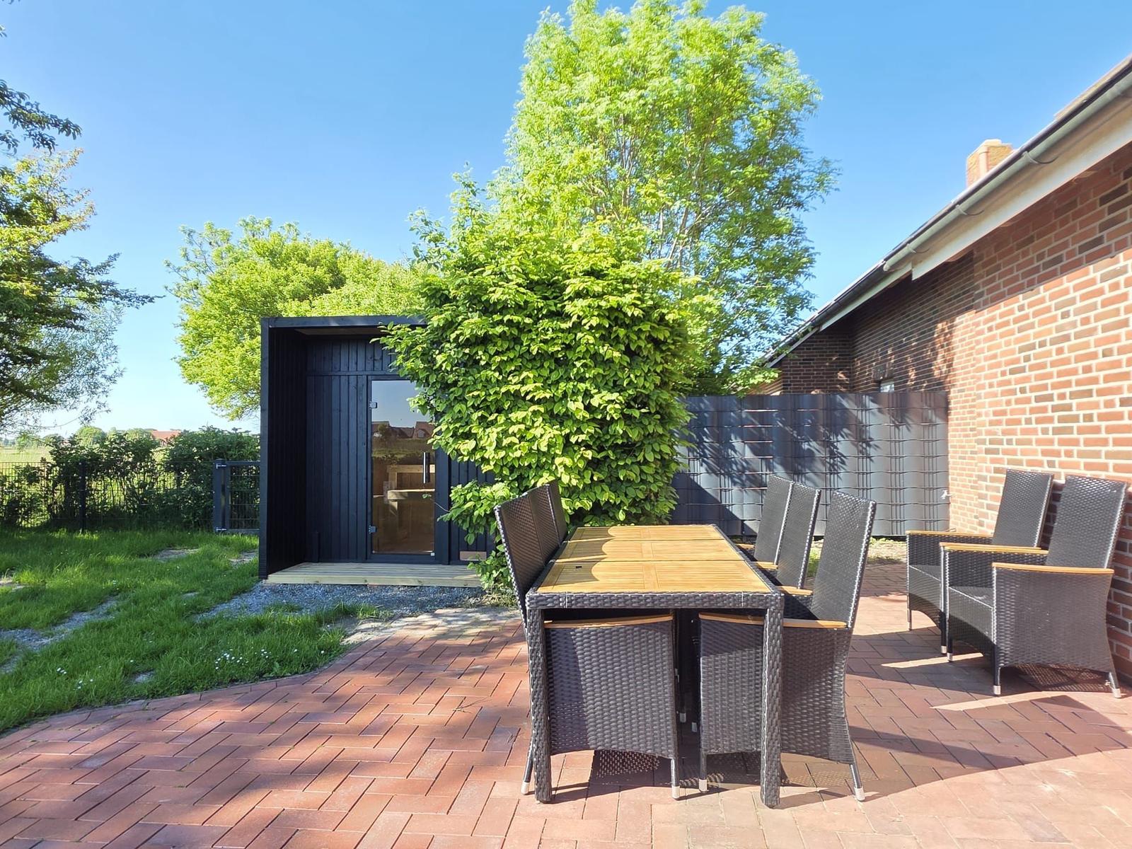 Terrasse mit Tisch und Stühlen neben einem Gartenhaus und Backsteinhaus.