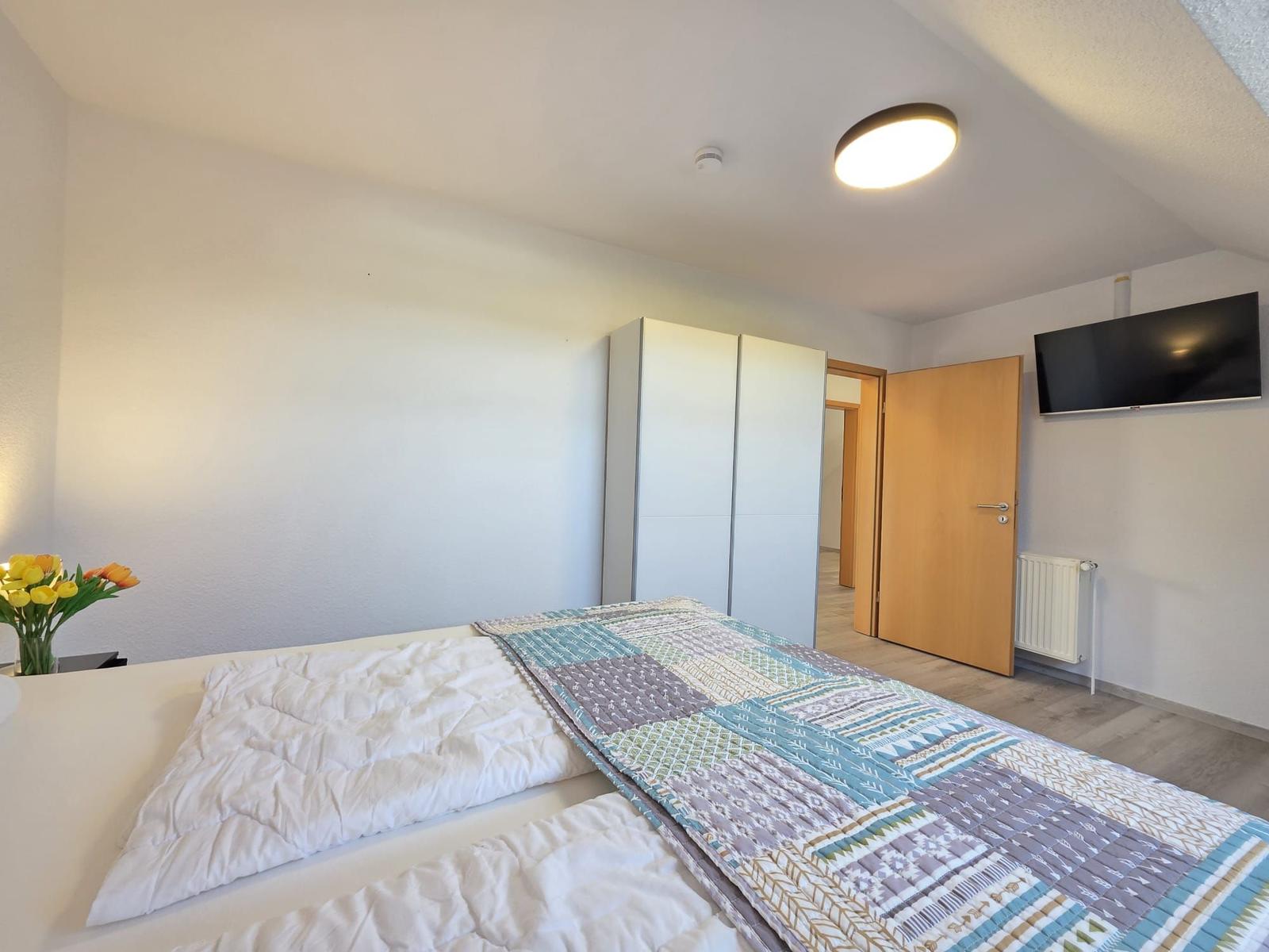 Schlafzimmer mit Bett, Kleiderschrank und Fernseher an der Wand.
