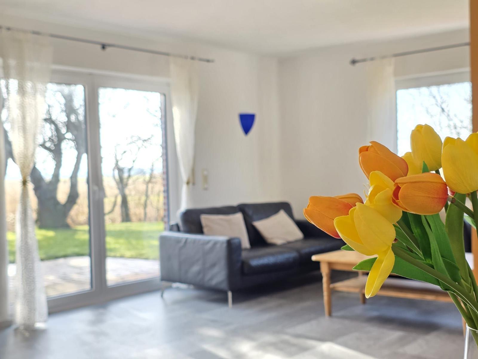 Wohnzimmer mit Sofa, Terrassentür und Tulpen im Vordergrund.