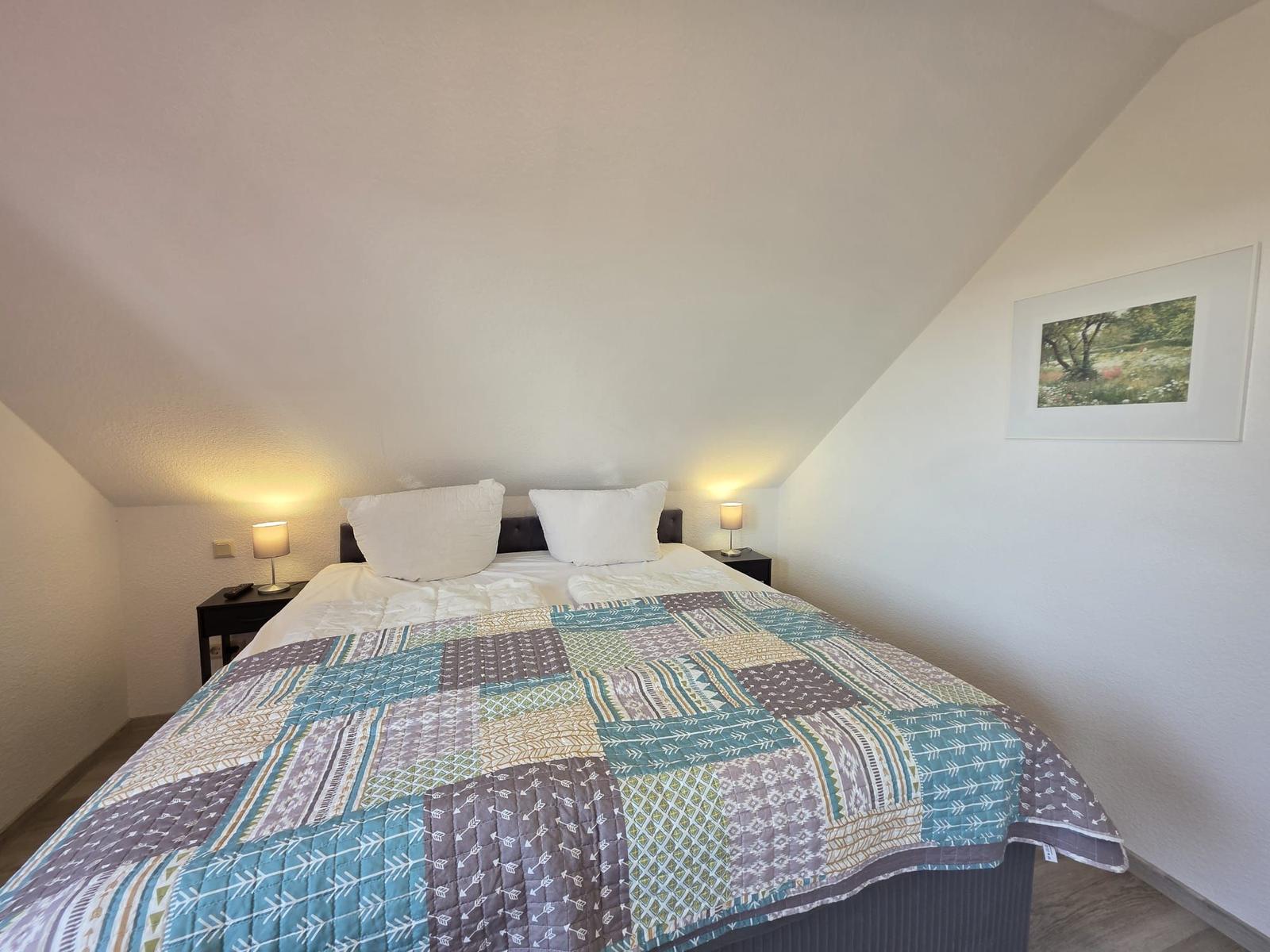 Schlafzimmer mit Doppelbett, zwei Nachttischen und einer Wanddekoration.