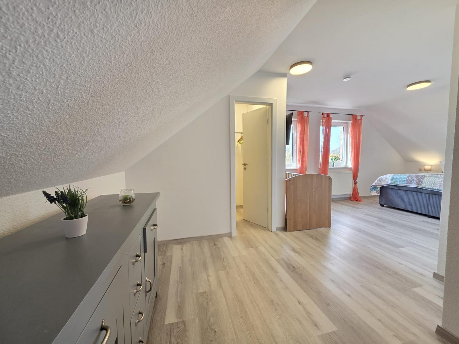 Schlafzimmer mit Dachschrägen, Holzboden und Fenster mit orangefarbenen Vorhängen.