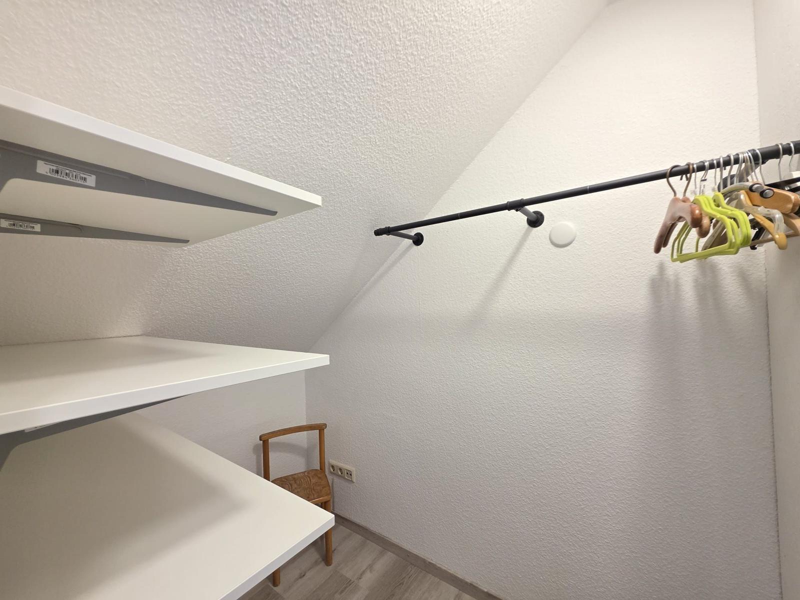 Kleiderstange mit Haken und weiße Regale in einem Dachbodenzimmer.