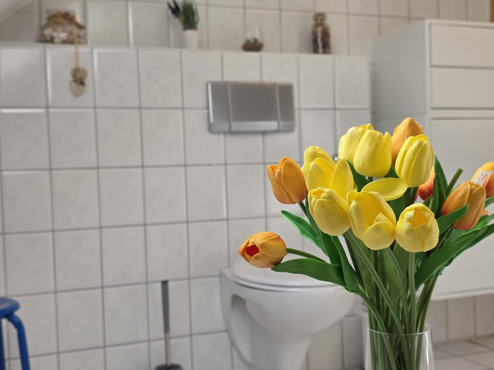 Badezimmer mit Toilette und Tulpen im Vordergrund.