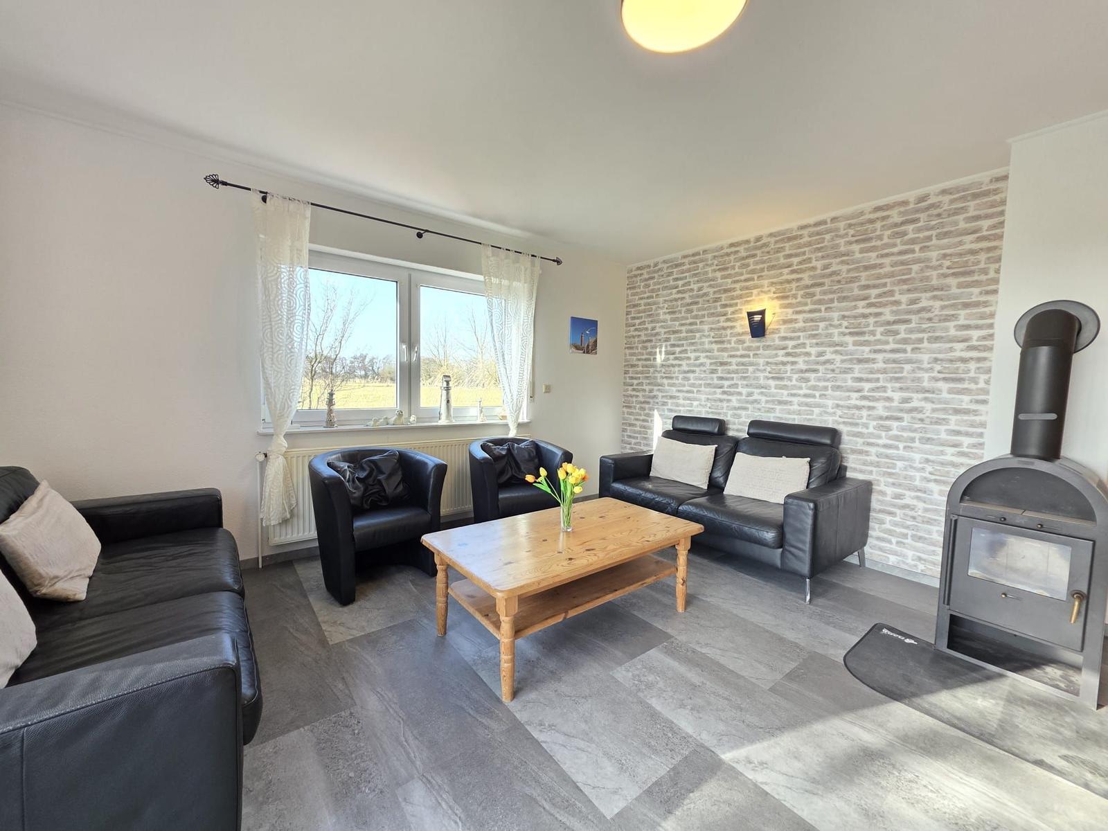 Wohnzimmer mit zwei Sofas, zwei Sesseln, Holztisch und Kaminofen. Wand aus Ziegelsteinen.