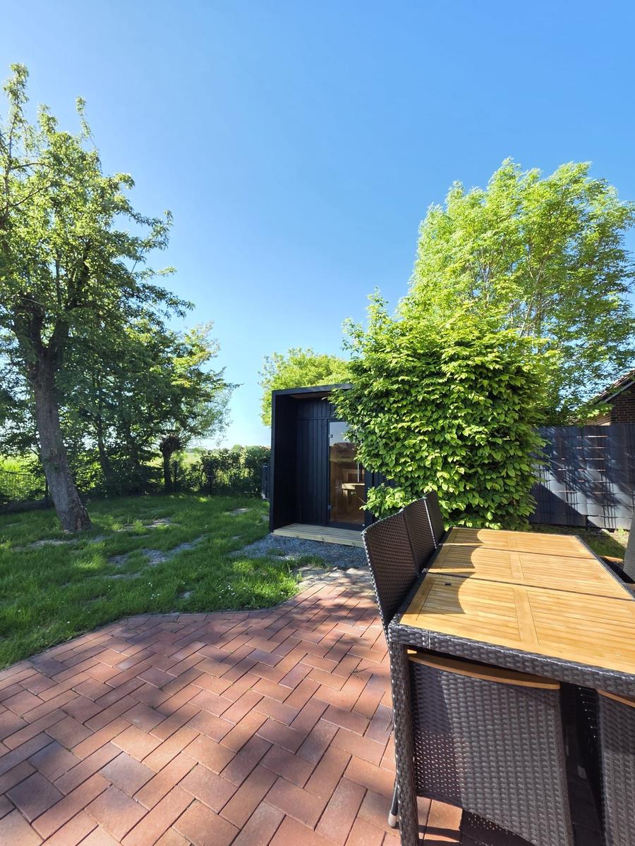 Terrasse mit Tisch und Stühlen, Blick auf moderne Hütte mit grünem Garten und Bäumen.
